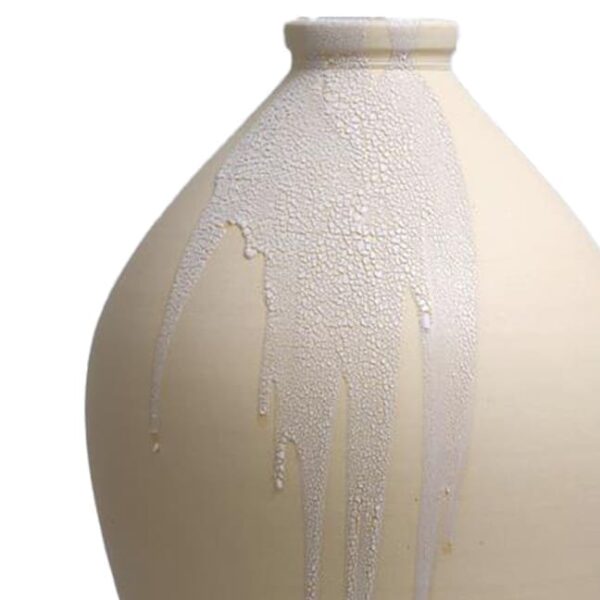 A close-up of a beige ceramic vase with white glossy glaze drips running down its surface.