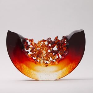 A semi-circular glass sculpture with smooth dark edges and a textured, amber-orange center, set against a plain white background.