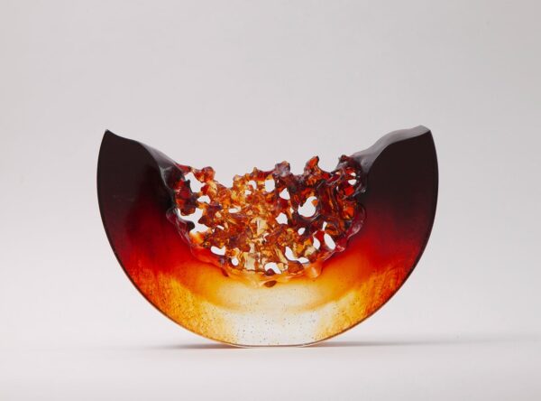 A semi-circular glass sculpture with smooth dark edges and a textured, amber-orange center, set against a plain white background.