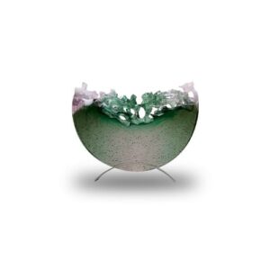 A semi-circular glass sculpture with a smooth lower half and a jagged, translucent green and pink upper edge, displayed on a simple metal stand.