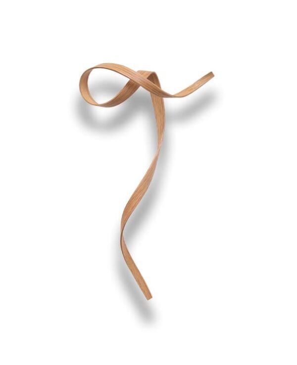 A single thin wooden strip is twisted into a loose, flowing ribbon shape on a white background, casting a soft shadow.