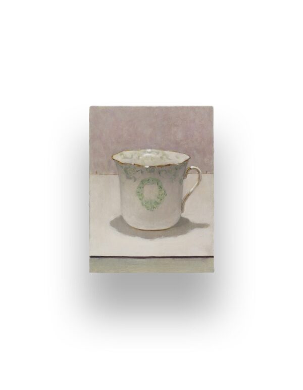 A single porcelain teacup with a green decorative pattern sits on a white surface against a muted, light-colored background.