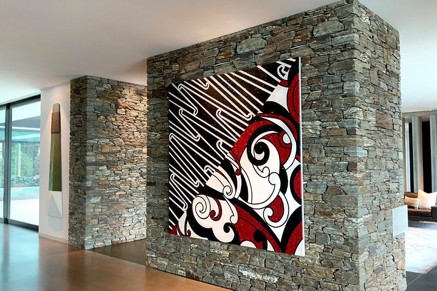 A stone wall in a spacious hallway displays an impressive large painting, along from it hangs a large wooden sculpture in the shape of a Māori adze.